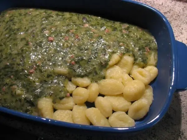 Gnocchi mit Spinat und Schinken liegen in einer blauen Auflaufform, überbacken und goldbraun gebräunt.