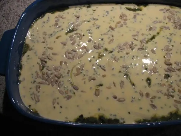 Ein Auflauf mit Gnocchi und Spinat ist in einer blauen Auflaufform zu sehen, bedeckt mit einer cremigen Schicht.