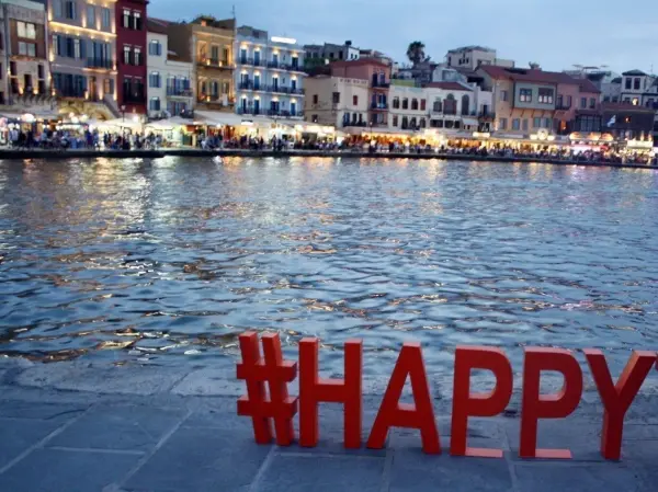 Rote Buchstaben mit der Aufschrift #HAPPY stehen am Ufer eines ruhigen Wassers während des Abenddämmerungslichts.