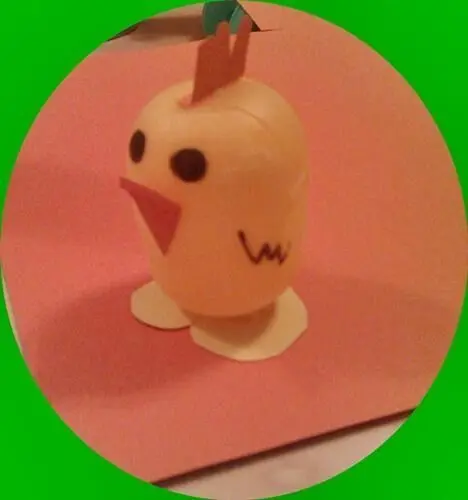 Ein gelbes Überraschungsei-Küken steht auf einem Tisch, mit Augen und Schnabel, umgeben von buntem Papier.
