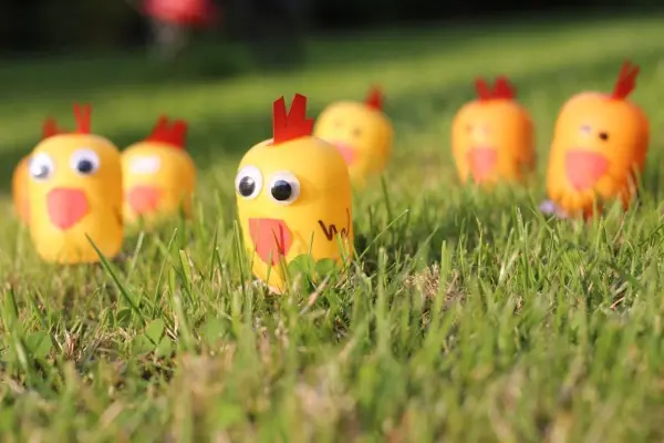 Gelbe Überraschungsei-Küken stehen auf grünem Gras und scheinen fröhlich zu quieken, umgeben von weiteren Küken.