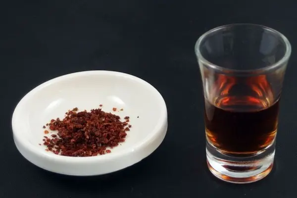 Rotem Pfeffer auf einem weißen Teller neben einem Glas Essig, das als Hilfe gegen scharfes Essen dient.