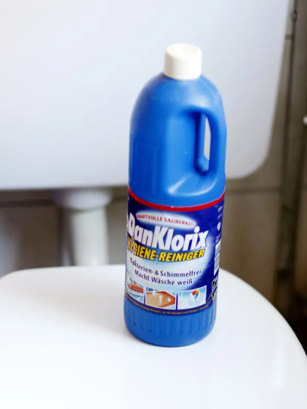 Eine Flasche DanKlorix-Reiniger steht auf einer weißen Toilettenschüssel, bereit zum Reinigen der Toilette.