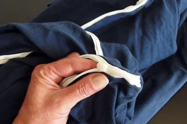 Eine Hand hält einen defekten Reißverschluss an einer blauen Bettwäsche, die verdreht auf einem Tisch liegt.
