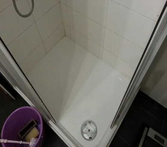 Eine saubere Dusche mit einem Abfluss in der Mitte und einem Eimer nebenan, bereit für die Dusche reinigen.