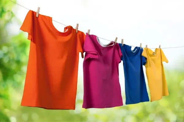 Bunte T-Shirts hängen frisch gewaschen an einer Wäscheleine im Freien, ideal zum Entfernen von Schweißgeruch.