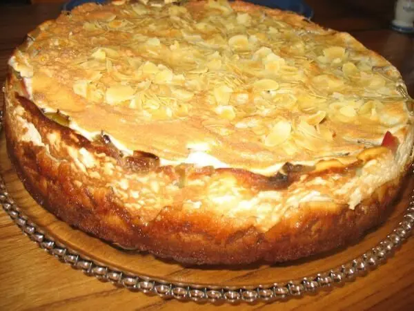 Eine Torte mit einer goldbraunen, knusprigen Mandelbaiser-Oberfläche liegt auf einem eleganten Tortenteller, umgeben von Holz.