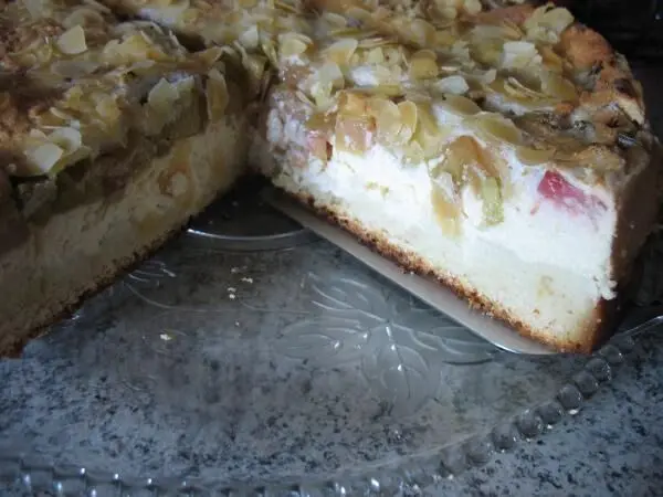 Eine Quark-Rhabarber-Torte mit knusprigem Mandelbaiser steht auf einem eleganten Glasuntersetzer.