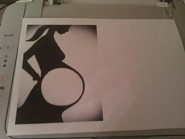 Silhouette einer schwangeren Frau auf Papier liegt auf einem Drucker, betont eine dekorative Darstellung der Schwangerschaft.