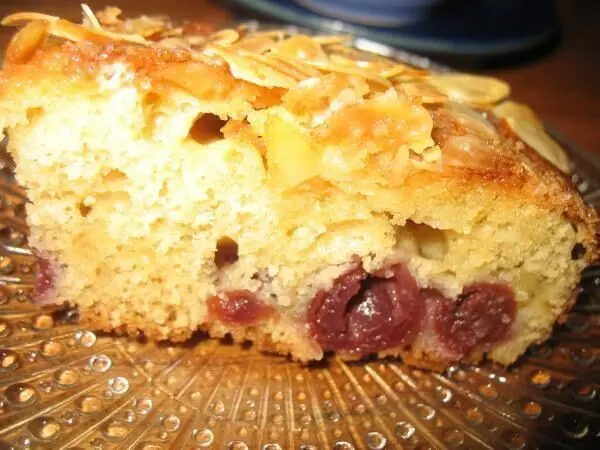 Ein saftiges Stück Buttermilch-Blechkuchen mit Kirschen liegt auf einem dekorativen Teller, umgeben von einem gemütlichen Ambiente.