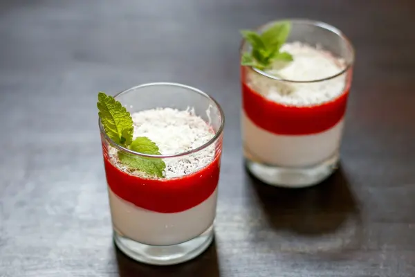 Zwei Gläser mit einem Mascarpone-Erdbeer-Dessert, mit roter Erdbeerschicht und frischer Minze, auf einem Holztisch.
