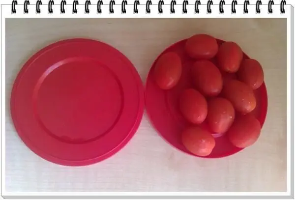 Cherrytomaten liegen auf einem roten Teller, bereit zum Halbieren, auf einem hellen Holztisch für einfaches Schneiden.