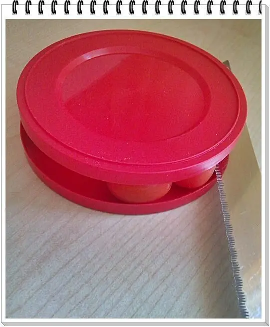 Ein roter Behälter hält Cherrytomaten zwischen Deckeln. Ein gezacktes Messer liegt daneben auf einem Holztisch bereit.