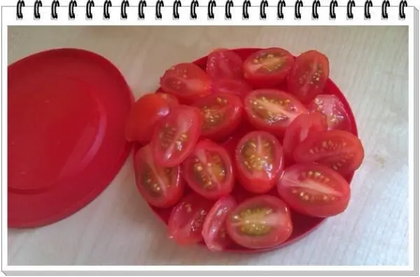 Cherrytomaten aufgeschnitten auf einem roten Teller, ruhend auf einem Holztisch, neben einem roten Deckel.