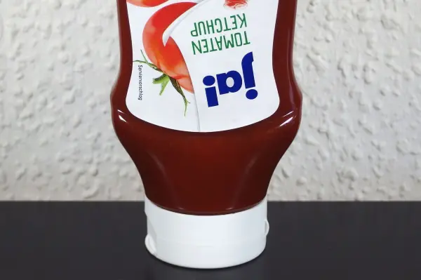 Eine Ketchupflasche steht aufrecht auf einem Tisch und scheint bereit zum Ausgießen des Tomatenketchups.