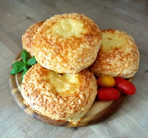 Käsebrötchen liegen golden braun auf einem Holzbrett, umgeben von bunten Tomaten und frischem Basilikum.