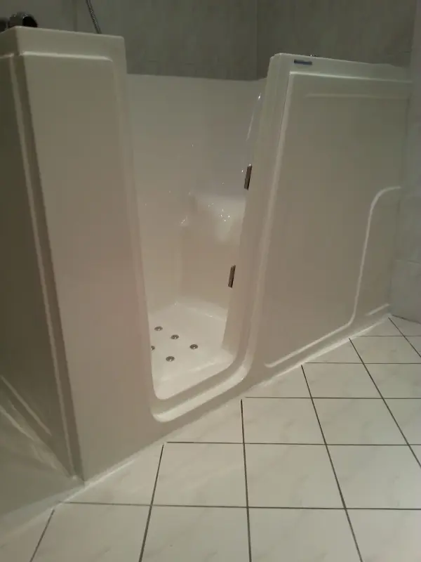 Eine Badewanne mit Einstiegshilfe steht bereit, um das Einsteigen in die Badewanne zu erleichtern, umgeben von hellen Fliesen.