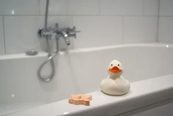 Eine Gummi-Ente sitzt auf der Badewannenkante, während ein Wasserhahn funktioniert und eine ruhige Badezimmerumgebung bietet.