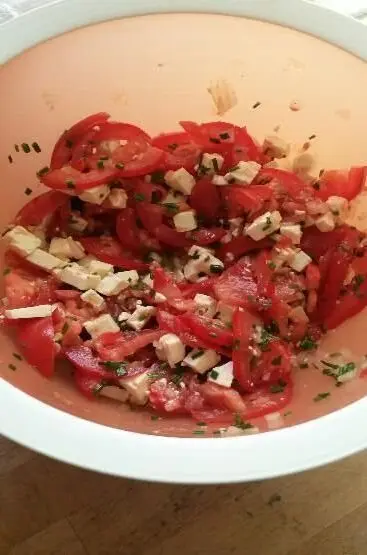 Eine Schüssel mit frischen Tomatenstücken und Limburger Käse, gewürzt mit Kräutern, bereit zum Servieren.