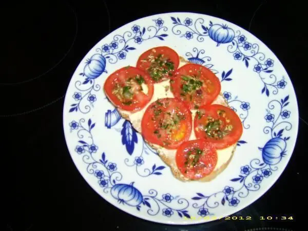 Ein Teller mit Molkebrot, belegt mit Tomatenscheiben und Kräutern, liegt auf einem mit blauem Blumenmuster verzierten Teller. Datum: 11/21/2012 10:34.