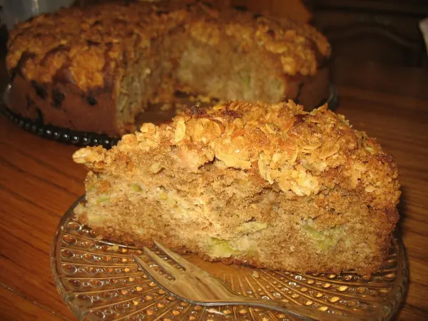 Ein Stück Rhabarber-Nuss-Torte mit einer goldbraunen Mandelkruste liegt auf einem Teller und sieht köstlich aus.