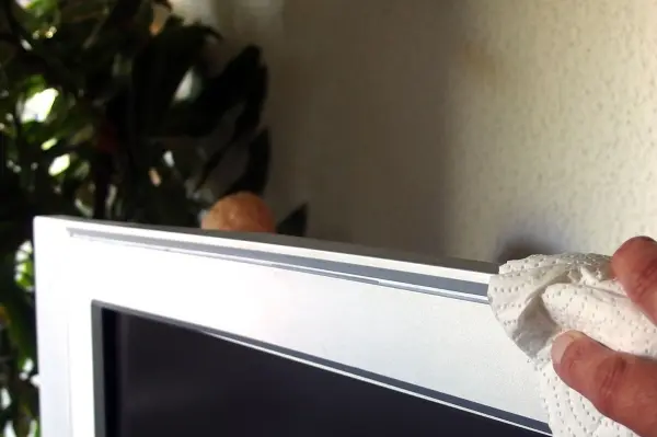 Ein Handtuch wischt die Kante eines Fernsehers ab, um Edding und Schmutz von glatten Oberflächen zu entfernen.