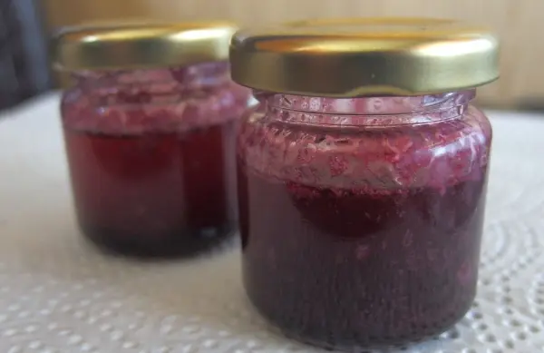 Zwei kleine Gläser mit Holunderbeeren-Butter stehen auf einem Tisch und zeigen eine tiefrote, süße Konsistenz.