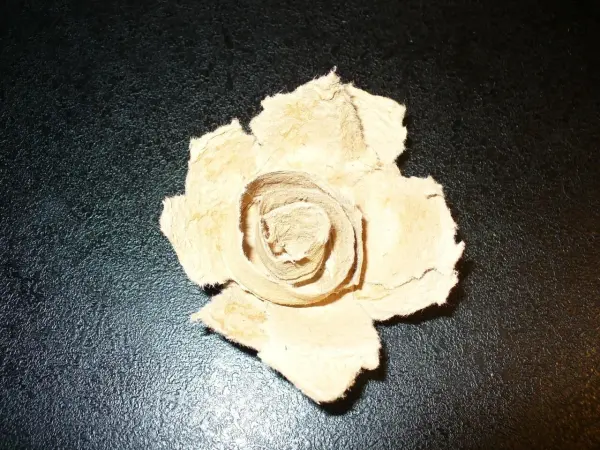 Eine Deko-Rose aus Eierkarton liegt flach auf schwarzem Untergrund, die Blütenblätter wirken strukturiert und handgemacht.