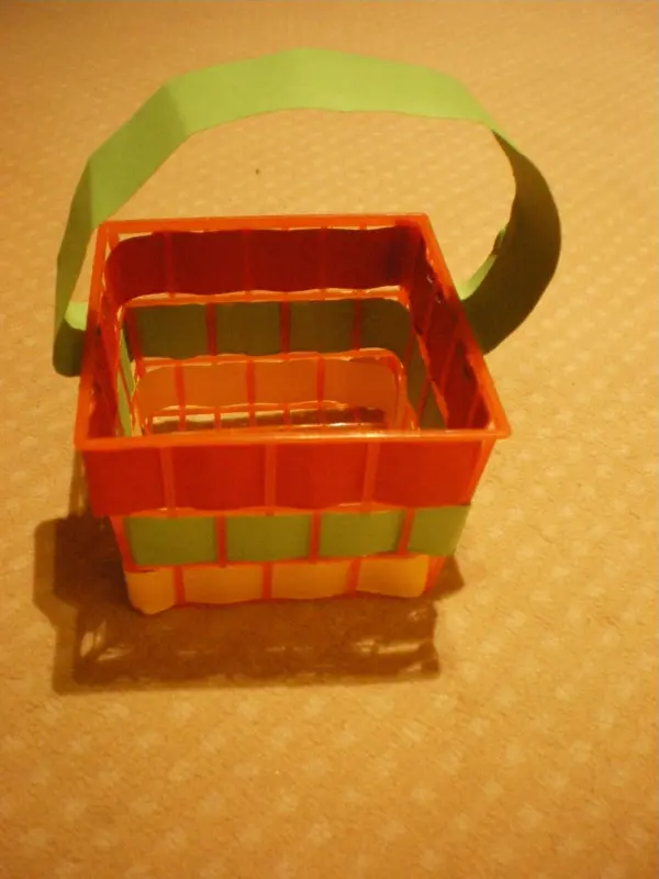 Ein buntes Körbchen aus Papppapier steht auf einer hellen Unterlage, bereit für den Kindergeburtstag.