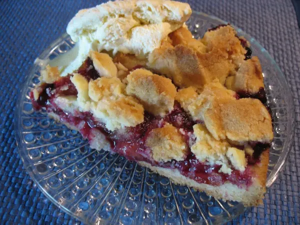 Eine köstliche Zwetschgen-Streusel-Torte auf einem Glasteller, serviert mit einer Portion Sahne, auf einem blauen Tisch.