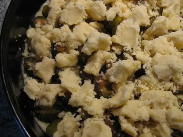 Eine Zwetschgen-Streusel-Torte mit goldbraunen Streuseln liegt in einer dunklen Backform und wartet auf den Backofen.