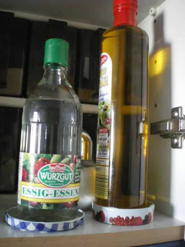 Zwei Flaschen, eine Essigflasche und eine Ölflasche, stehen auf bunten Untersetzern im Küchenschrank.
