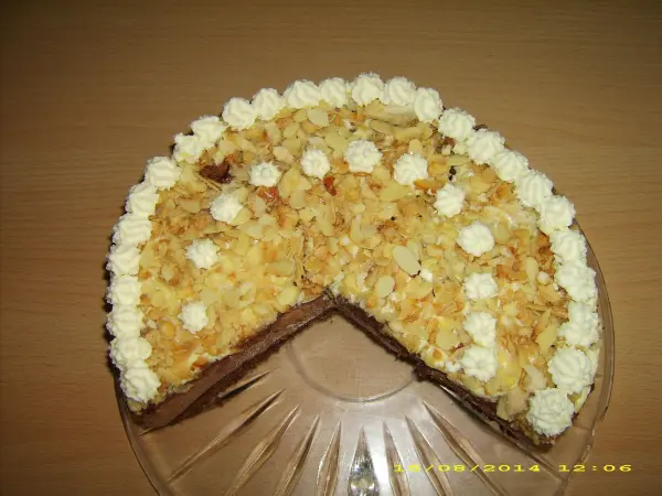 Eine Schoko-Käsesahne-Torte mit Sahnehaube steht auf einer Glasplatte in einem hellen Raum.
