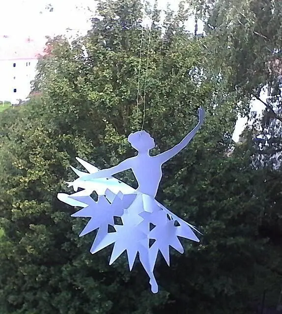 Papier-Ballerina hängt elegant vor üppigem, grünem Hintergrund und dient als stilvolle Dekoration.