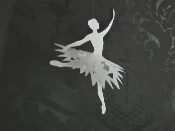 Eine filigrane Ballerina schwingt elegant in einem dekorativen Umfeld, umgeben von dunklen, floralen Mustern.