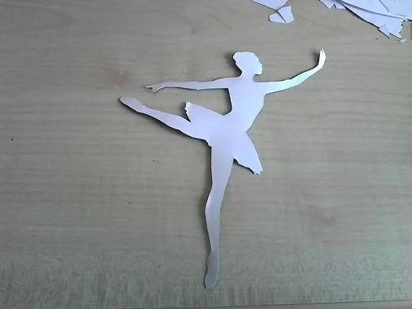 Eine ausgeschnittene Ballerina steht auf einem Tisch und zeigt eine elegante Pose, umrahmt von weiteren Papierstücken.