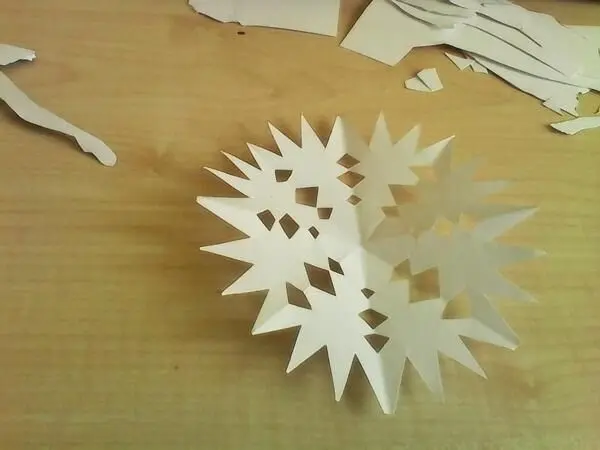 Eine filigrane, weiße Dekoration in Form einer Ballerina sitzt kreativ auf einem Tisch, umgeben von ausgeschnittenem Papier.
