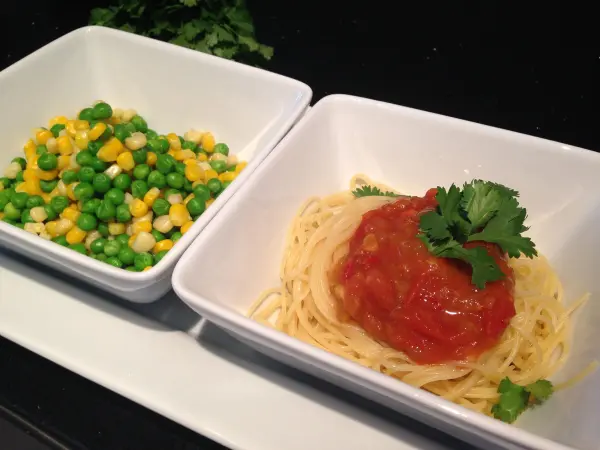 Pasta mit Tomaten-Chutney liegt appetitlich in einer Schüssel, neben einer Portion buntem Gemüse auf einem weißen Teller.