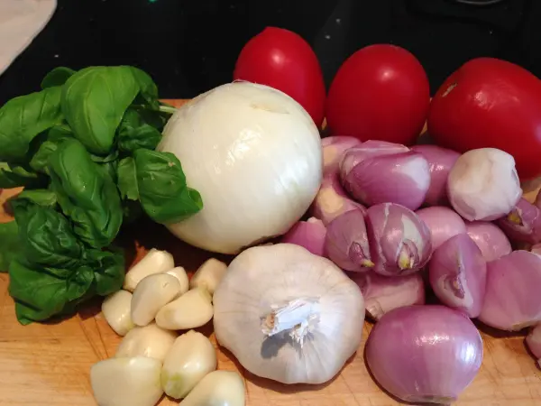 Bunte frische Zutaten wie Tomaten, Zwiebeln und Basilikum liegen ordentlich auf einem Holzbrett zur Zubereitung von veganem Spaghetti-Chutney bereit.