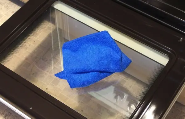 Eine blaue Reinigungstuch liegt auf einer sauberen Glas-Ofentür, während sie zum Reinigen vorbereitet wird.