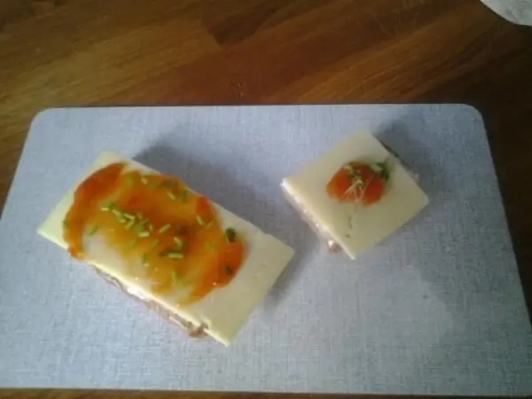 Zwei belegte Brotscheiben mit Käsescheiben und feurig-süßem Paprikamus, dekoriert mit Schnittlauch, auf Schneidebrett.