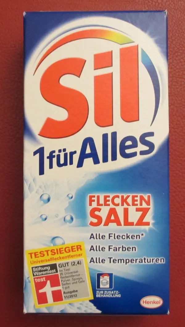 Eine blaue Verpackung von Sil 1-für-Alles-Flecken-Salz zeigt die vielseitige Anwendung als Universal-Fleckentferner. Text: "TESTSIEGER", "Alle Flecken*", "Alle Farben", "Alle Temperaturen".
