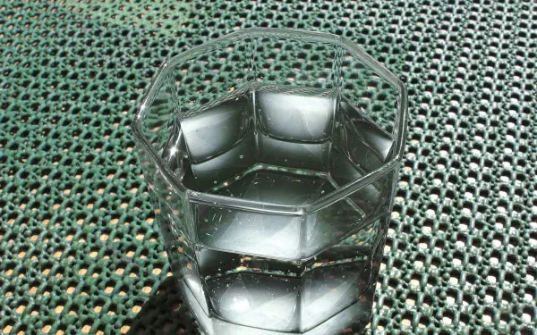 Ein klarer Glas mit Wasser steht auf einer strukturierten Oberfläche aus grünem Material und reflektiert Licht.