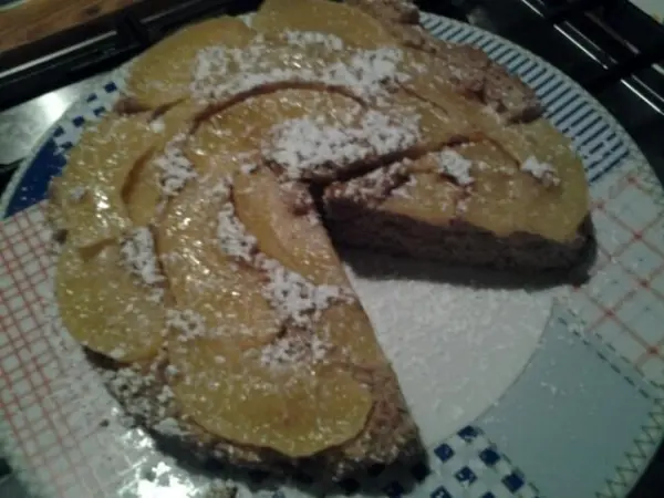 Ein appetitlicher, glutenfreier Apfel-Mandelkuchen mit Puderzucker steht auf einem Teller, umgeben von einer Küchentheke.