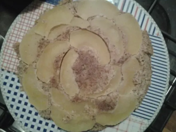 Ein glutenfreier Apfel-Mandelkuchen liegt auf einem Teller, dekorativ mit Apfelscheiben belegt, in einer hellen Küche.
