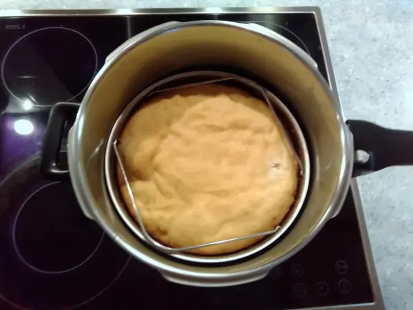 Ein glutenfreier Apfel-Mandelkuchen ist im Schnellkochtopf auf einer Röstgitterablage sichtbar, umgeben von einer modernen Kochumgebung.