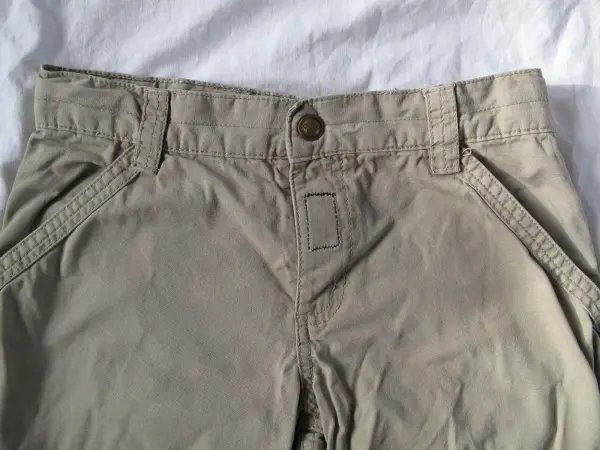 Beige Kinderhose mit defektem Reißverschluss auf einem weißen Untergrund, bereit zum Ersetzen durch Klettband.