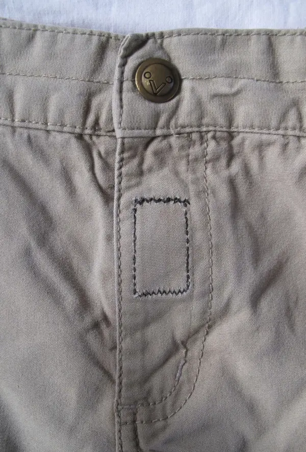 Eine Kinderhose mit einem knappen Reißverschluss, der durch Klettband ersetzt werden soll, liegt flach auf einem Untergrund.