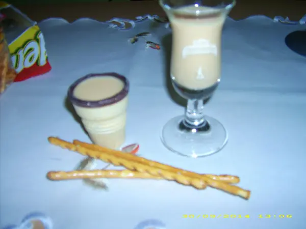 Ein Sahnelikör steht in einem Glas und einem kleinen Becher auf einem Tisch, umgeben von Snack-Stäbchen.