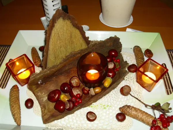 Eine herbstliche Tischdekoration aus Naturmaterialien zeigt eine Holzscheibe in einer eleganten Anordnung mit Kerzen und Frucht.